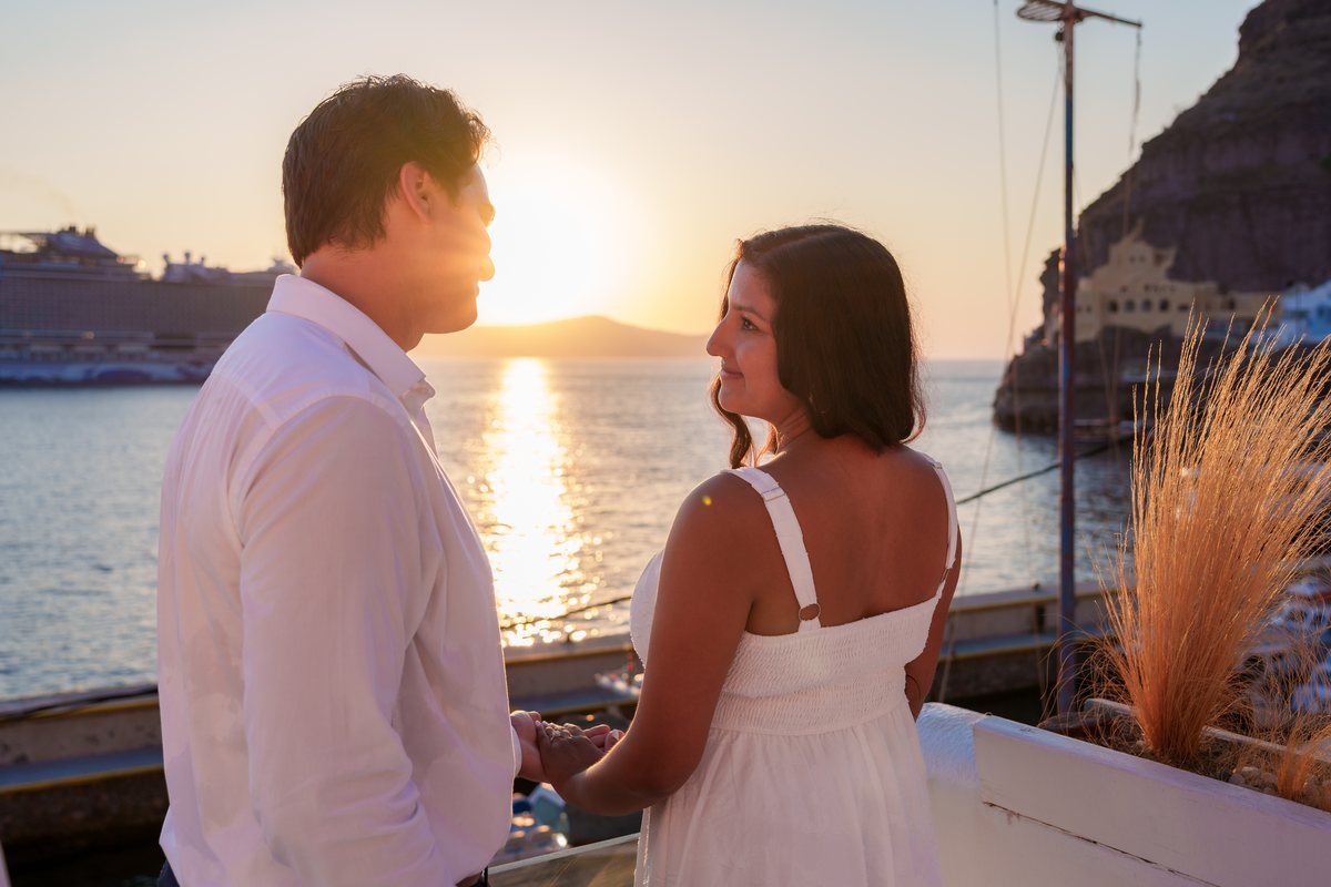 The Aegean at golden hour from AION's rail — the sun on the water, the Fira cliff above the old port