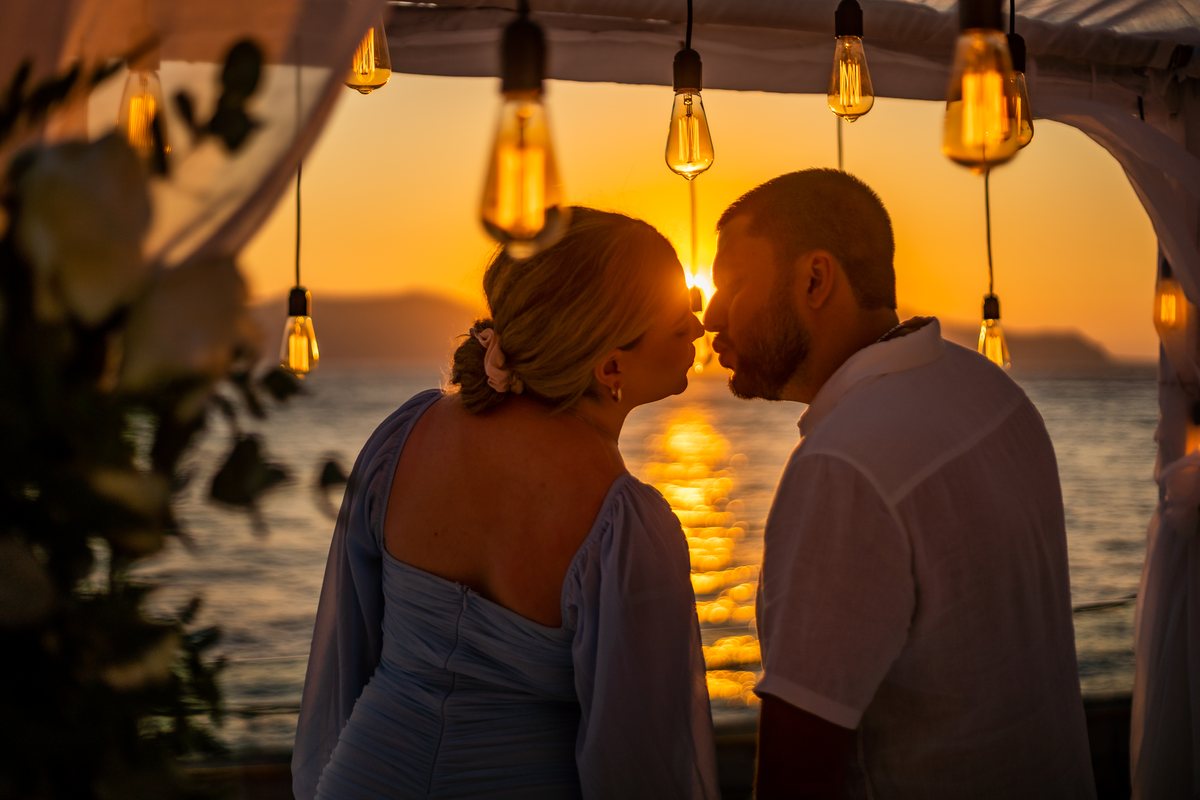 Two people at AION's rail in the last of the sun, bulbs strung overhead