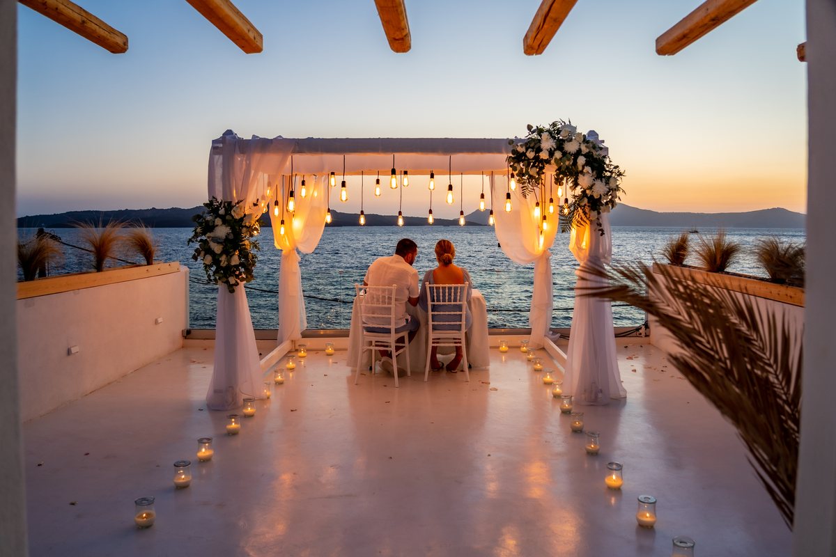 AION's ceremony arch dressed in white drapes and flowers, a couple at the table as the sun goes down