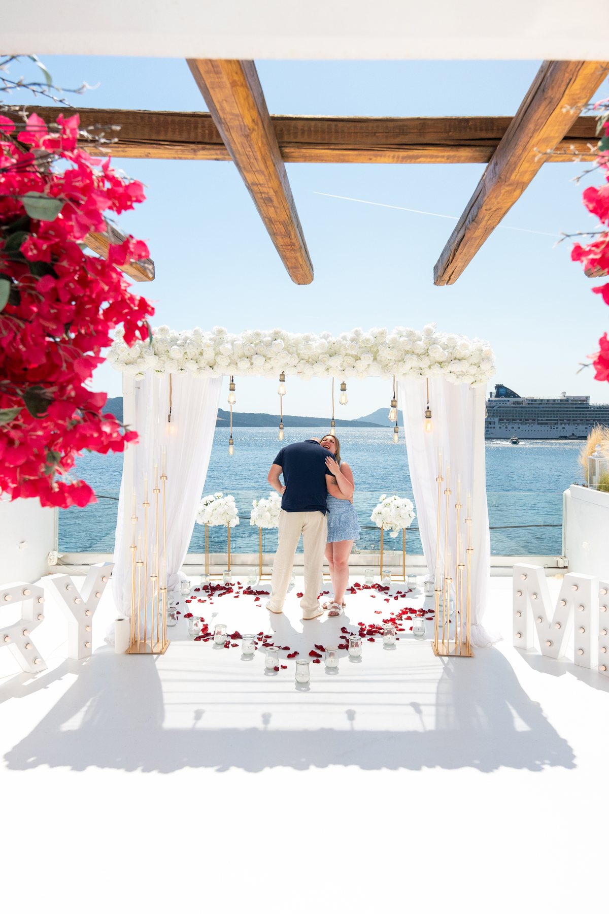 The white arch at AION framed by bougainvillea, petals down the aisle to the caldera