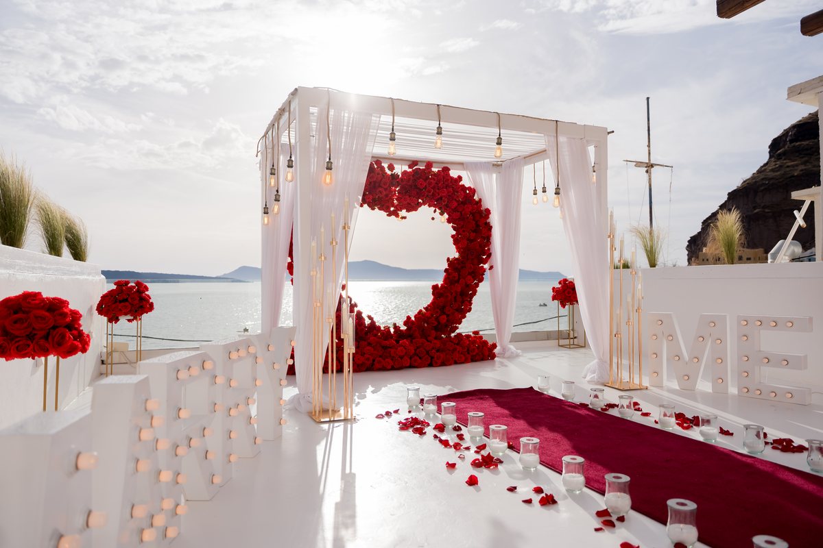 AION's terrace set for a proposal — the red rose heart under the white canopy, candles and petals, the sun flaring through the drapes