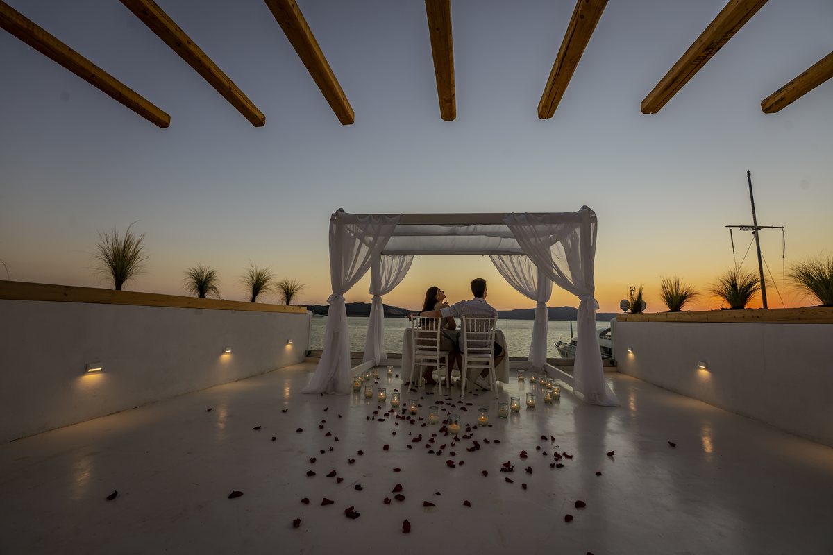 The private dinner table set on AION's terrace, candles and petals across the floor at dusk