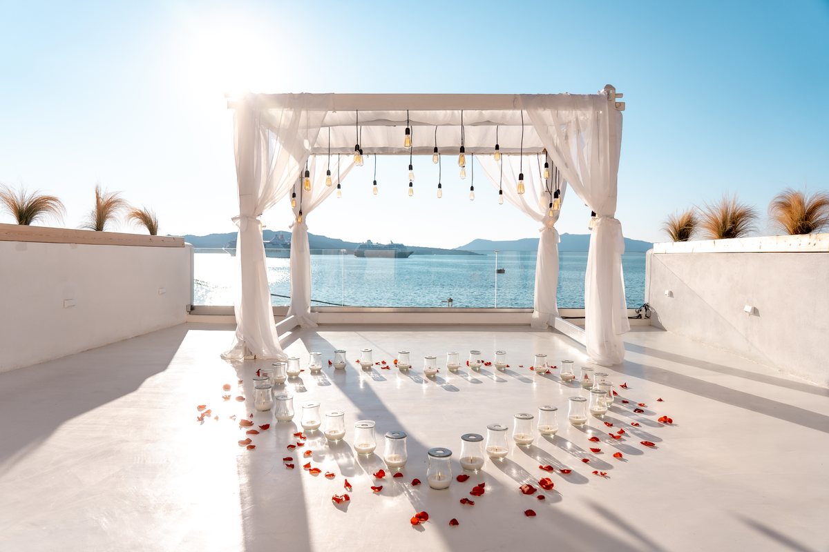 A proposal set-up under AION's white-draped arch, rose petals down the terrace to the sea