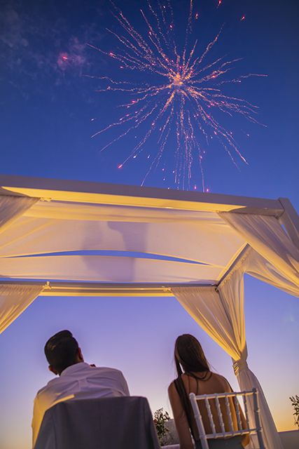 Fireworks bursting in the dusk sky above the ceremony arch while a couple watches from their table at AION