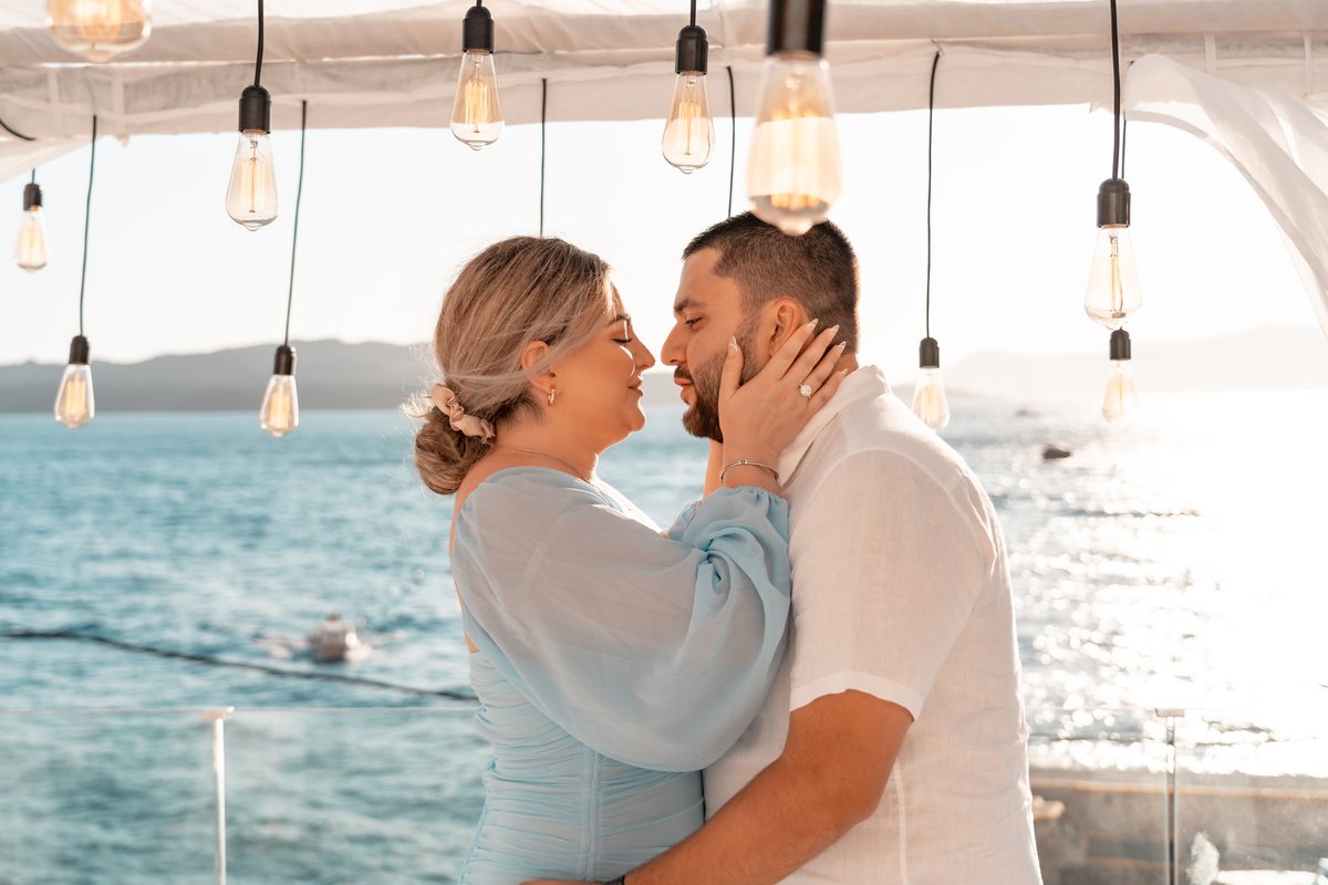 George and Amalya together under the hanging bulbs on AION's terrace after the proposal