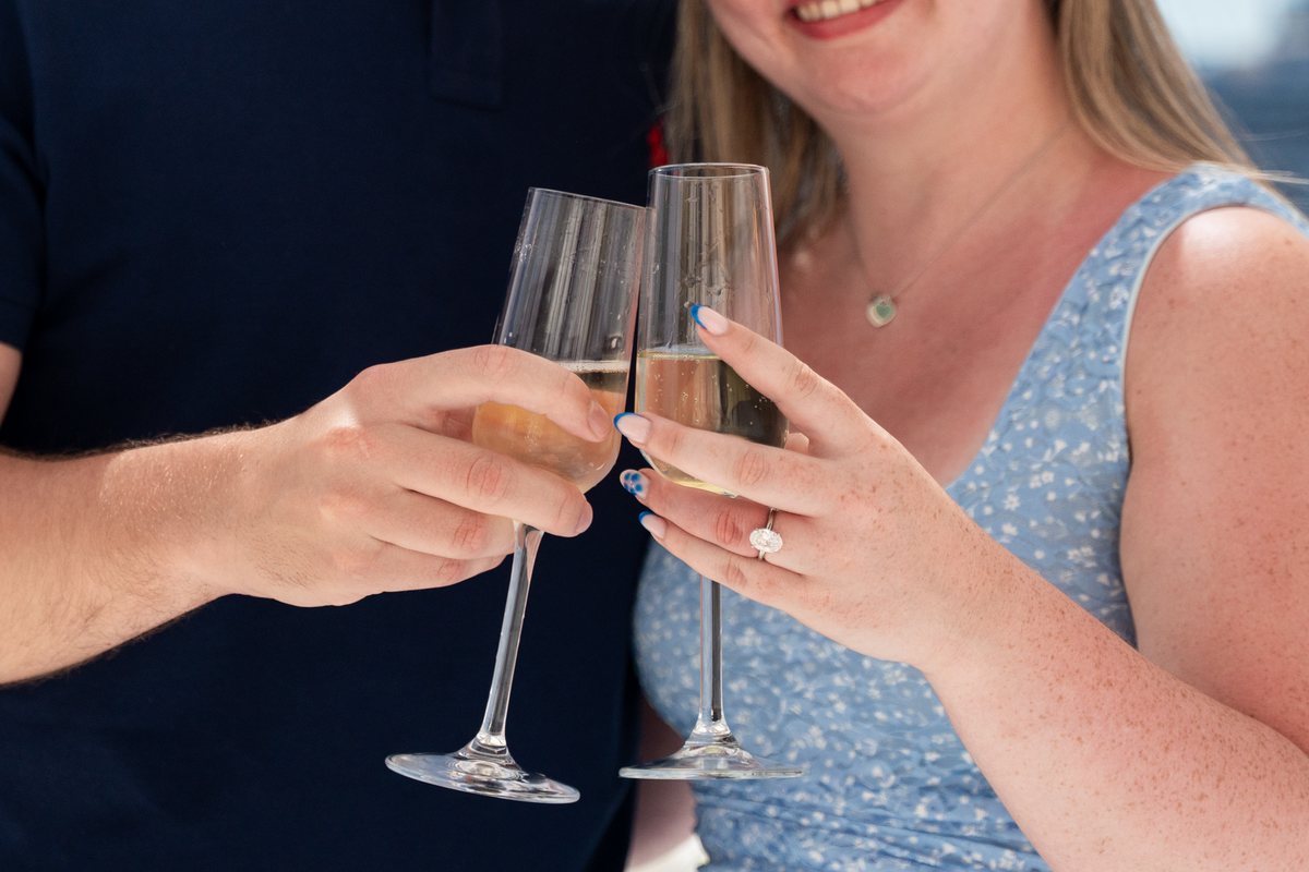 Two champagne flutes touching after a proposal at AION Santorini, the new ring catching the light