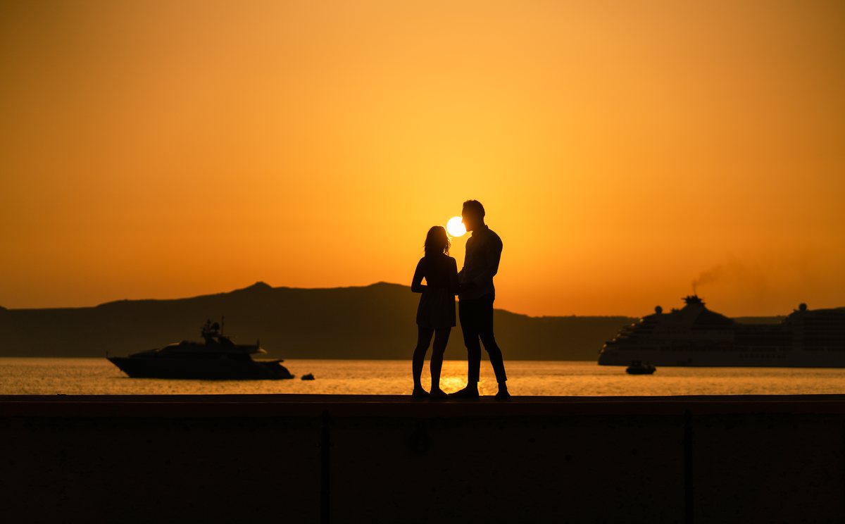A newly engaged couple in silhouette against the Santorini sunset below AION