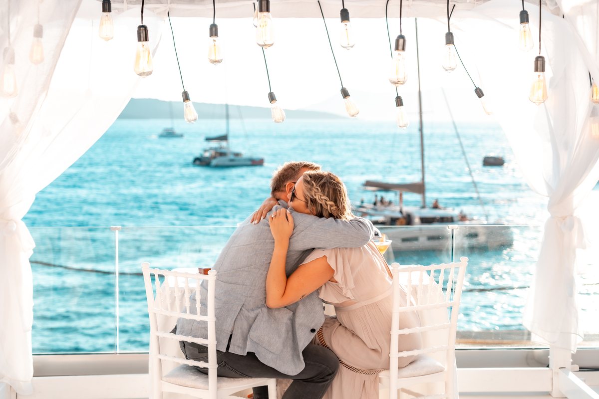A private cocktail hour on AION's terrace, catamarans moored on the caldera below