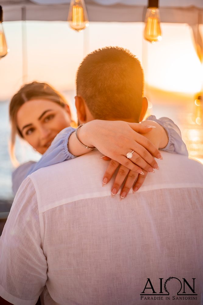 Her arms around him at the dinner table, the new ring catching the light