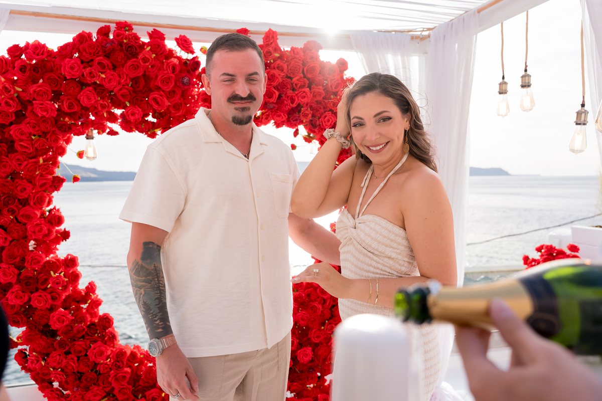 Champagne poured beside the red rose heart arch on AION's terrace, minutes after the proposal