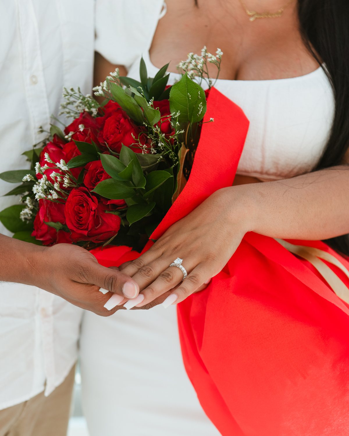 A bouquet of red roses and two hands with a fresh engagement ring at AION Santorini