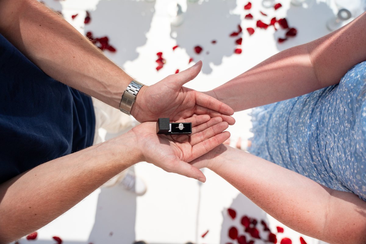 The ring going onto her finger at AION's Santorini proposal venue, rose petals on the terrace floor