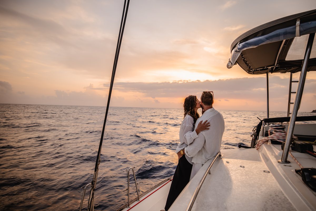 A couple on the bow of a catamaran crossing the caldera at sunset, headed for the old port at AION