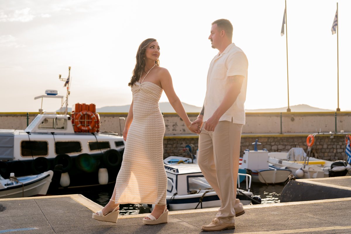 A couple walking in to AION along the old port quay, fishing boats beside them