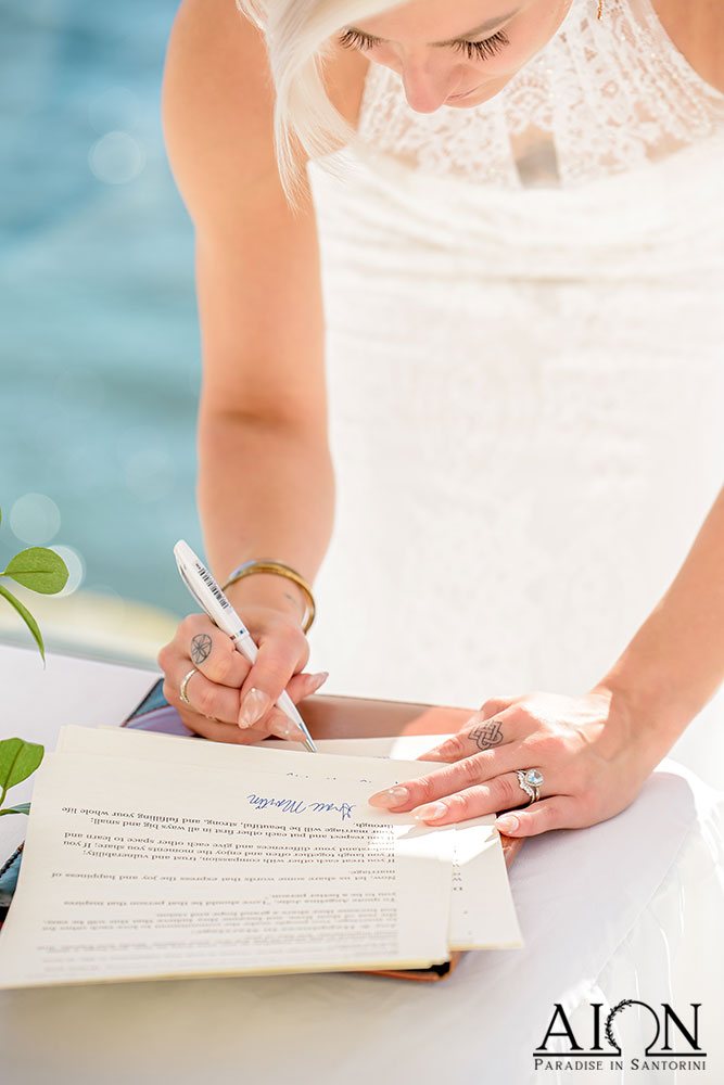 A bride signing the marriage register at AION Santorini, the Aegean behind her