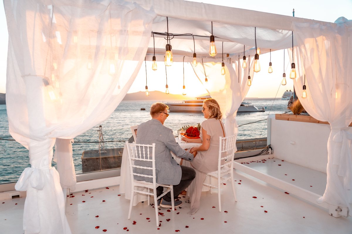 The table styled for two on AION's terrace — white cloth, rose petals, curtains moving in the wind